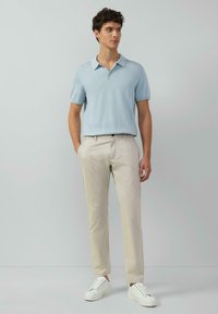 Hellblaues Polohemd mit kurzen Ärmeln, beigefarbene, schmal geschnittene Chinos und weiße Sneaker. Glatte Baumwollstruktur mit klassischem Kragen design.