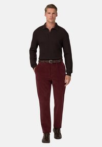 Brun långärmad polo med en strukturerad mönster, kombinerad med mörk burgundy byxor och ett flätat brunt bälte. Bruna sneakers fulländar looken.