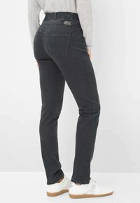 Pantaloni in denim neri con design affusolato, vita elastica e tasche posteriori. Indossati con sneakers bianche, mostrano un look casual.