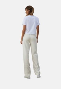 Witte cropped t-shirt en crème wijde-pijpen broek. Glad katoenen stof, losse pasvorm, subtiele stikseldetails en elastische tailleband aan de broek.