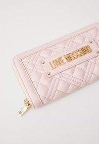 Λεωφορείο ροζ πορτοφόλι από συνθετικό υλικό, με χρυσή πλάκα που αναγράφει "LOVE MOSCHINO", συμπληρωμένο με χρυσά στοιχεία και φερμουάρ.