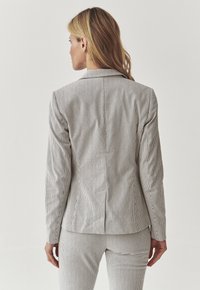 Gestreifter, taillierter Blazer in Hellgrau und Weiß, ausgestattet mit einem klassischen Kragen und einem einzigen Rückenschlitz, kombiniert mit passenden Hosen.