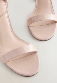 Sandali open-toe in rosa blush con una fascia ampia e lucida sul piede e un design slanciato e curvo per un aspetto minimalista.