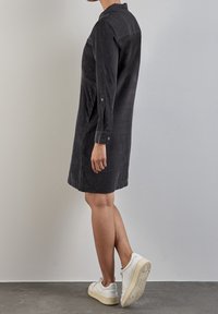 Abito camicia in cotone a coste nera con maniche lunghe e spacchi laterali, abbinato a sneakers bianche. Tessuto morbido, dettaglio colletto e bottoni decorativi.