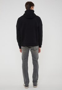 Felpa nera con cappuccio a sacco e coulisse, abbinata a jeans in denim grigi e sneakers casual.