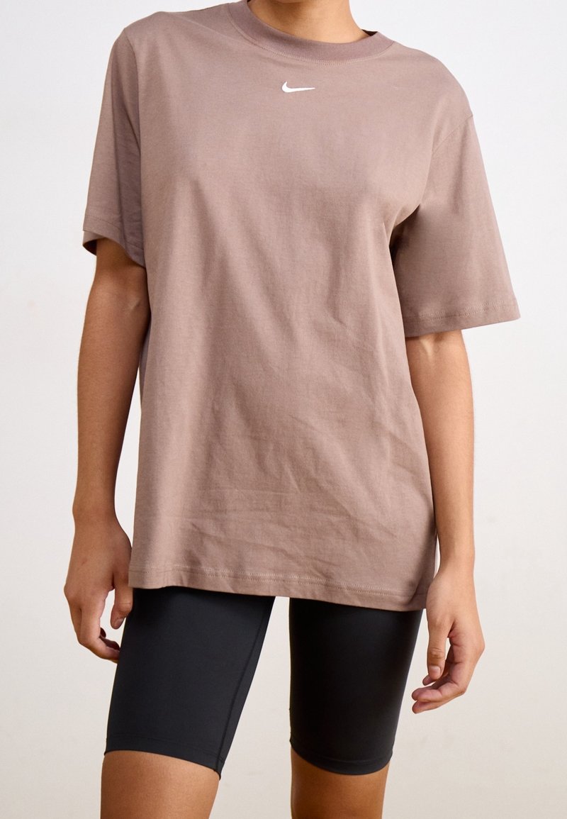 Brun bomullströja med rund halsringning, med en liten vit Nike-logotyp på bröstet. Matchas med svarta cykelbyxor.