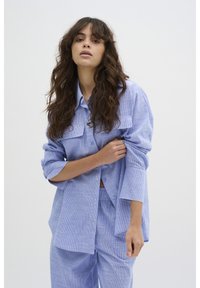 Cămașă cu dungi alb-albastre, cu nasturi, două buzunare pe piept, croială lejeră și mâneci lungi, asortată cu pantaloni matching. Textură de țesătură moale.