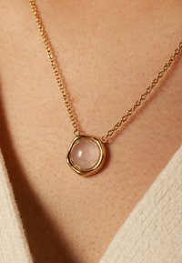 Gouden ketting met een ronde, transparante roze steen gezet in een organische, ronde zetting. Soepele metalen schakels en delicate textuur.