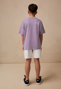 Fioletowa, oversizeowa koszulka, białe szorty, czarne sneakersy. Materiał bawełniany, okrągły dekolt, krótkie rękawy, gładka, bez wzorów ani zdobień.