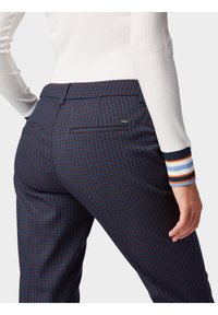 Granatowe spodnie w kratę w czerwono-niebieskim kolorze, z tylnią kieszenią z małym metalowym logo oraz prążkowanym białym topem z paskowymi akcentami.