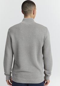 Lys grå ribbestrikket genser med høy hals, lange ermer og en avslappet passform. Den teksturerte stoffet gir et mykt utseende.