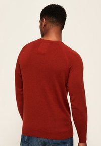 Maglione borgogna con maniche lunghe, colletto a giro e una sottile texture. Presenta un piccolo patch quadrato sul retro. Realizzato in materiale lavorato a maglia.