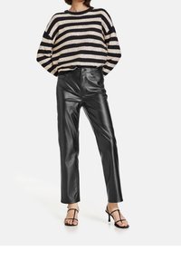 Zwart-beige oversized gebreide trui met strepen en een ronde hals, gecombineerd met zwarte, hooggetailleerde nepleren broek en zwarte sandalen met bandjes.