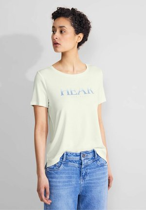 T-shirt vert clair à manches courtes avec un texte graphique "ÉCOUTE LA MER" en bleu. Associé à un jean taille haute bleu, en tissu lisse et à coupe décontractée.