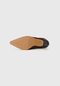 Brown suede heel with a pointed toe, textured sole, and a shiny black accent at the back. Smooth finish with slight curve at the heel.