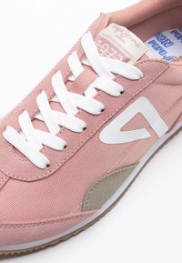 Baskets en tissu et suède rose avec lacets blancs, logo blanc sur le côté et accent beige en suède près de la semelle.