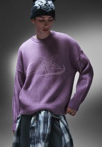 Maglione rigato viola con un design a stella in una tonalità più chiara. Abbinato a una camicia a quadri annodata in vita e a un berretto con motivo.