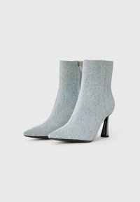 Stivaletti ankle blu chiaro in texture denim con accenti scintillanti, punta affusolata e tacco sottile. Chiusura con cerniera sul retro.