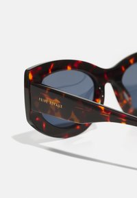 Óculos de sol de tartaruga com uma armação larga em forma de olho de gato, lentes azul-escuras e logotipo dourado "PRIVÉ REVAUX" na haste.