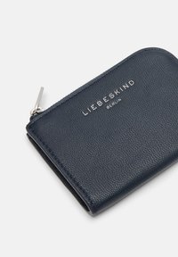 Granatowy skórzany portfel o fakturowanej powierzchni, z srebrnym zamkiem błyskawicznym i wytłoczonym logo, w kształcie prostokąta i o prostym designie.