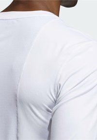 Vit sporttröja i slät tyg med strukturerade meshpaneler på axlarna. Har en åtsittande passform och minimala sömmar för komfort.