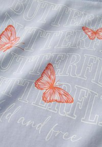 Tela azul claro con grandes letras blancas que dicen "MARIPOSA" y ilustraciones de mariposas naranjas, con el texto "salvaje y libre" debajo en cursiva.