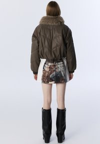 Bruine leren bomberjack met een gequilte patroon en faux fur kraag, gecombineerd met een mini rok met denimprint en zwarte kniehoge laarzen.