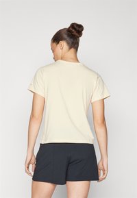 Beżowy T-shirt z krótkim rękawem, bawełniany, luźny krój, okrągły dekolt, widok z tyłu, zestawiony z czarnymi szortami, minimalistyczny design, bez wzorów.