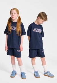 Mörkblå bomullströja och shorts-set med grafiskt tryck. Matchas med blå sneakers och vita ankelsockor. Avslappnad passform och rak skärning.