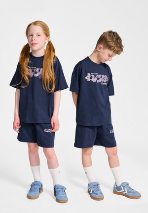 Mörkblå bomullströja och shorts-set med grafiskt tryck. Matchas med blå sneakers och vita ankelsockor. Avslappnad passform och rak skärning.