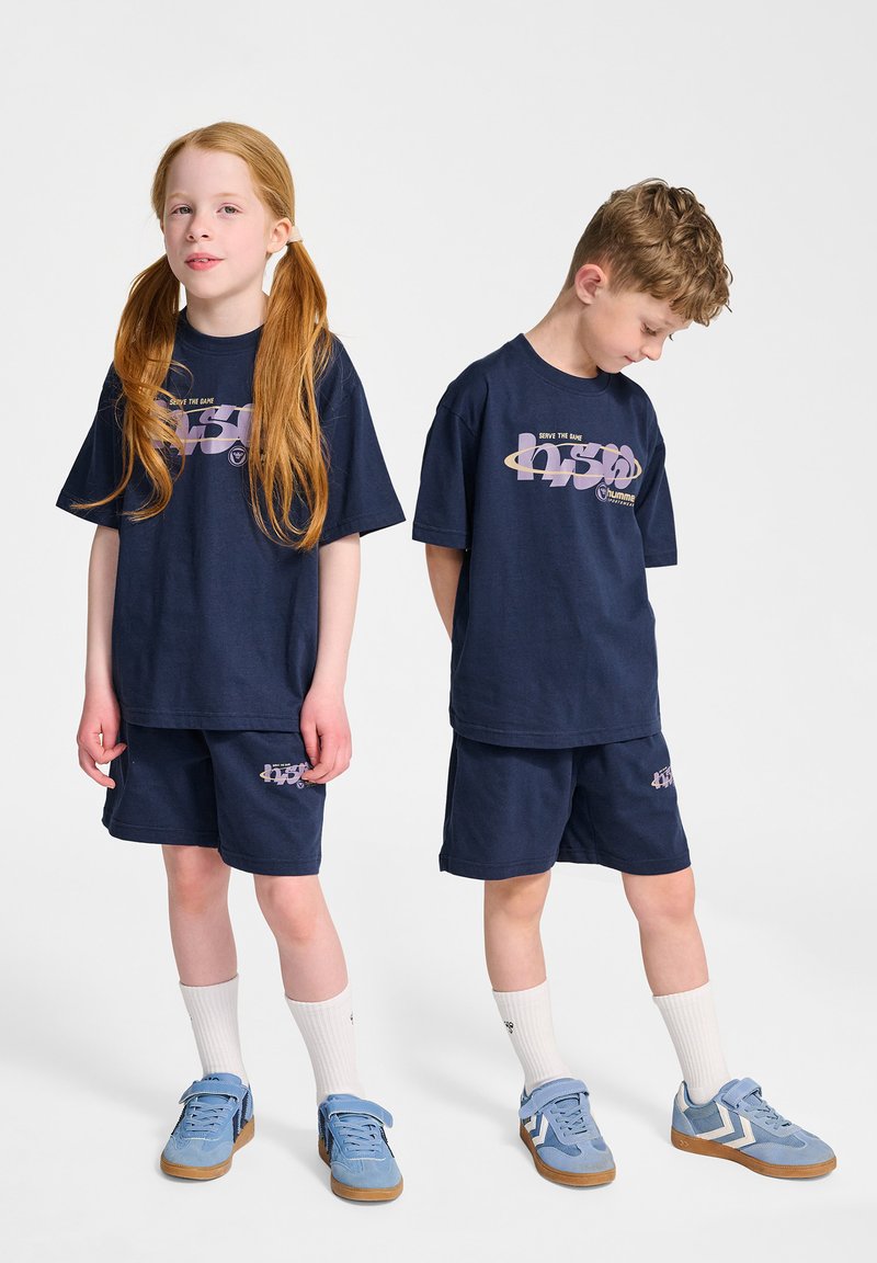 Mörkblå bomullströja och shorts-set med grafiskt tryck. Matchas med blå sneakers och vita ankelsockor. Avslappnad passform och rak skärning.