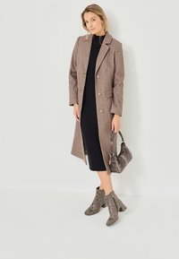 Brown wool long coat with large buttons, black ribbed dress, and snake-print ankle boots. Black and grey patterned handbag completes the look.
