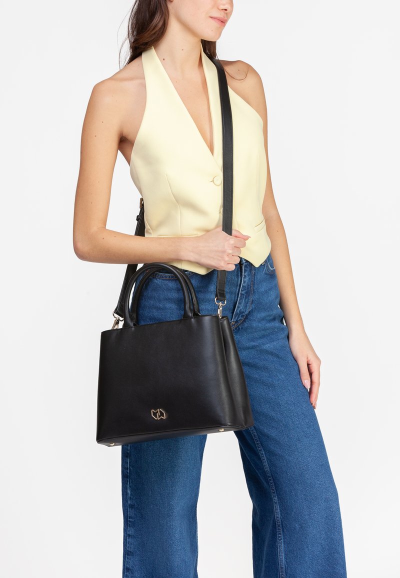 Borsa a mano in pelle nera con doppio manico e tracolla regolabile. Presenta un emblema dorato e una forma rettangolare strutturata.