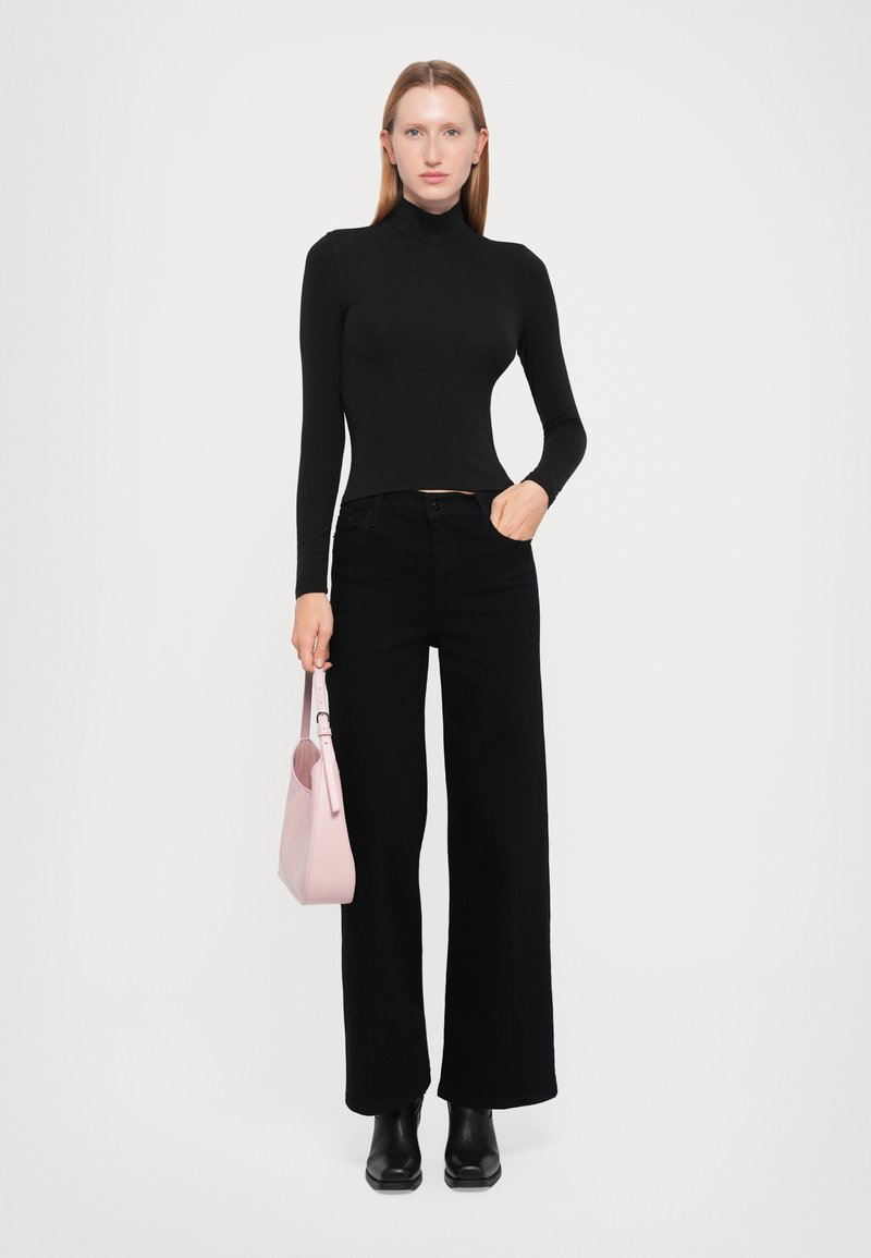 Un pull à col roulé noir à manches longues, un pantalon large noir taille haute, des bottines noires, et un sac à main rose clair avec une bandoulière.
