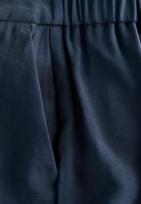 Mornarskoplavi materijal s glatkom teksturom, s nabranim detaljima i elastičnom čvrstom gumicom. Bez vidljivih uzoraka ili metalnih dijelova.
