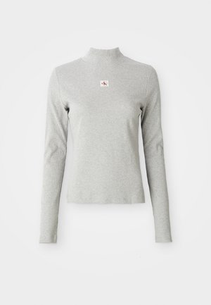 Grijze langemouwen coltrui van zachte stof, met een geribbelde textuur en een klein CK-logo in een witte vierkant op de borst.