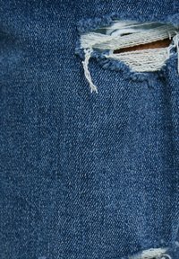 Denim fabric with a medium blue hue, featuring a distressed rip with frayed edges, exposing lighter inner material.