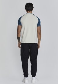 Heren overhemd met korte mouwen, met een crèmekleurig lijf en blauwe raglanmouwen en een gestructureerde afwerking nabij de manchetten. Gecombineerd met zwarte broeken.