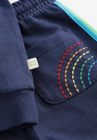 Pantaloni di cotone blu navy con vita elastica, dotati di una tasca decorata con archi ricamati a colori dell'arcobaleno e una piccola etichetta.
