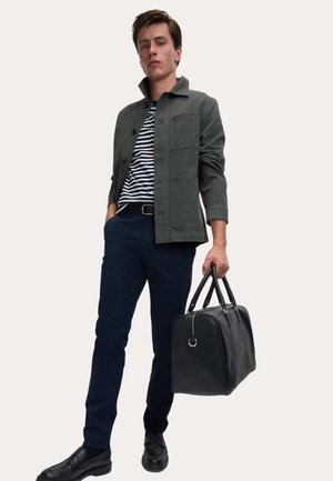 Grijze blousejas over een gestreept shirt, marineblauwe broek, zwarte schoenen, met een zwarte leren totebag. Eenvoudig ontwerp en neutrale kleuren.