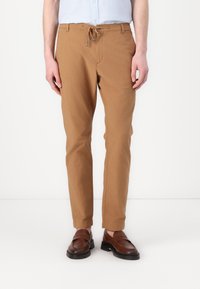 Brune bomullsbukser med snøring i livet, innsnevret ben og en myk tekstur. Brukes sammen med mørkebrun lær slip-on sko.