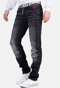 Jeans in denim nero con vestibilità slim, con dettagli rigati e cuciture rosse. Indossati con sneakers bianche e una felpa grigia.
