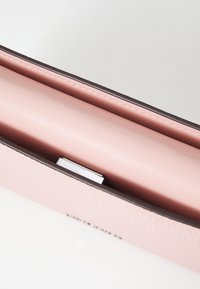 Rosa läderklutch med en texturerad yta, kontrasterande mörk kant, magnetisk stängning och slät insida. Minimalistisk design med rena linjer.