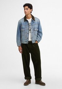 Ανοιχτό μπλε τζάκετ από τζην με σκούρο πράσινο κολάρο από κοτλέ, δύο τσέπες στο στήθος, συνδυασμένο με σκούρες πράσινες παντελόνες από κοτλέ και καφέ μπότες.