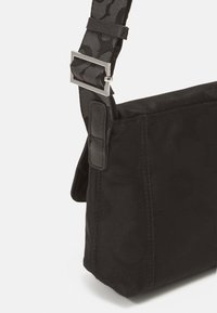 Black crossbody bag with a textured fabric, featuring a patterned design. Adjustable strap with metallic hardware. Compact shape.