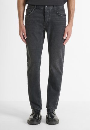 Jeans en denim noir avec une coupe droite, un léger dégradé, un design à cinq poches et une fermeture à bouton en métal, associés à des bottes en cuir noires.