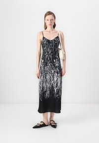 Zwart-wit mouwloos jurkje met een vloeiende rok, voorzien van een vloeibare print en een v-hals. Gecombineerd met zwarte ballerina's en een kleine tas.