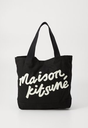 Black canvas tote bag with white cursive text "Maison Kitsuné" on the front. Features sturdy, matching black fabric handles.