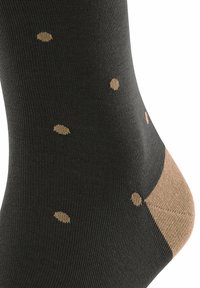 Schwarze Socke mit einem beigen Polka-Dot-Muster und einem beigen Akzent an der Ferse. Hergestellt aus einem glatten, dehnbaren Material.