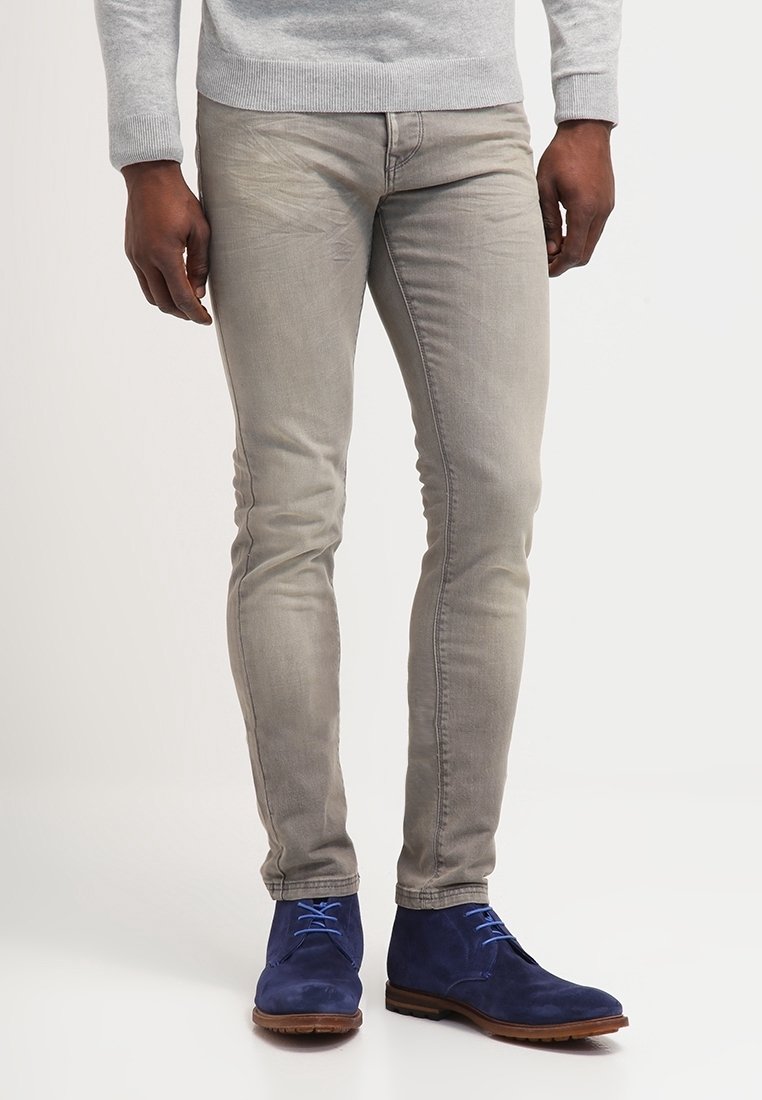 Jeans slim-fit grigio chiaro in denim, abbinati a stivaletti alla caviglia in suede blu con lacci blu. Il pullover è grigio chiaro, con scollatura a girocollo.